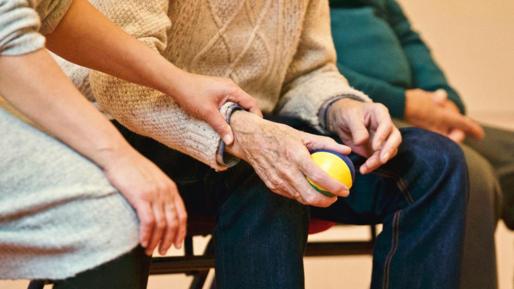 pexels-photo-339620-339620 An elderly person receives support from a caregiver, holding hands indoors, showcasing compassion.
